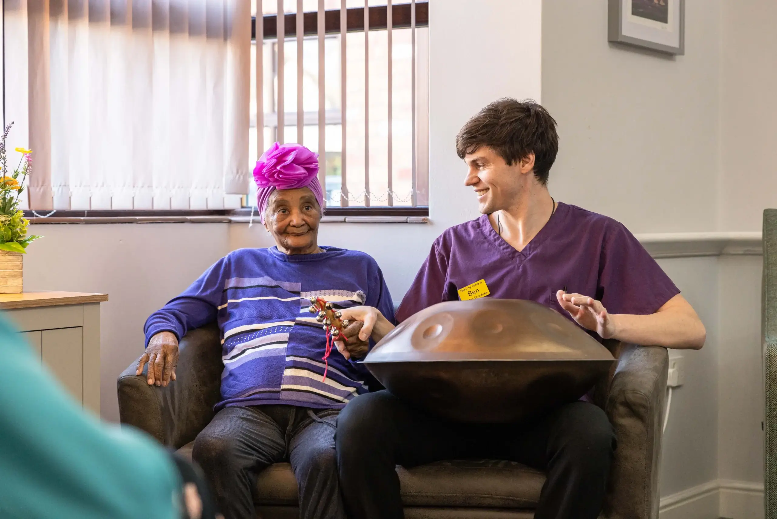 elderly woman and caregiver playing handpan drum together, both smiling and engaged